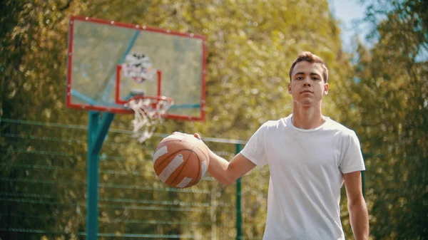 Un joven parado en un campo de deportes y golpeando la pelota desde el suelo — Foto de Stock