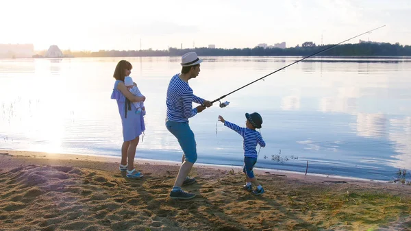 Familienangeln am Ufer des Flusses bei Sonnenuntergang - Mann und Frau mit zwei Kindern — Stockfoto