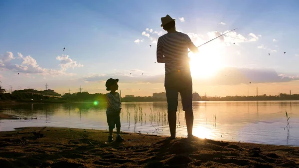 Батько і син рибалять на березі річки в промені сонця - Дитина посміхається - Птахи літають в небі — стокове фото
