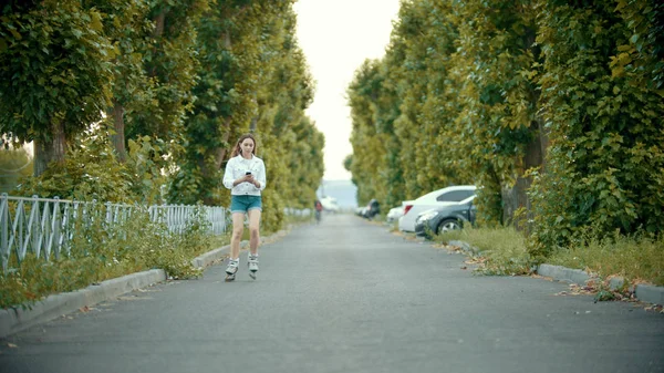 Una ragazza adolescente in pattinaggio sui pattini sulla strada - guardando il telefono — Foto Stock