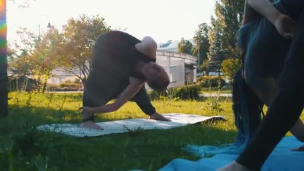 Mujer joven con rastas haciendo yoga en el parque con el instructor - doblando en poses — Vídeos de Stock