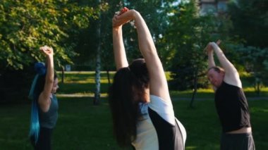 Eğitmenleri ile parkta yoga yapan iki genç kadın - ellerini kaldırın ve yanlara bükme - mavi dreadlocks ile bir kadın