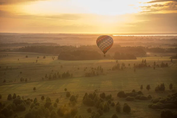 A colorful air balloon flying over the field - bright sunset — Stock Photo, Image