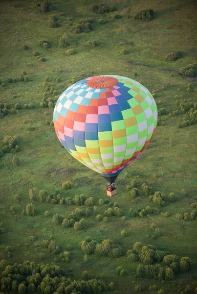 En stor farverig ballon flyver over den grønne felt ved hjælp af varme teknologi - Stock-foto