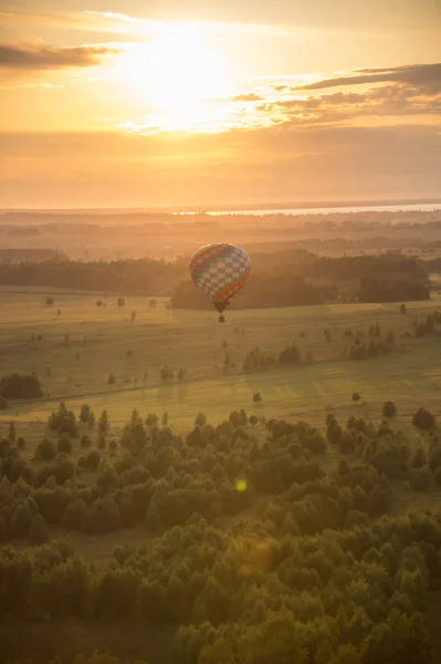 Un globo aerostático volando sobre el bosque y el campo - puesta de sol brillante — Foto de Stock