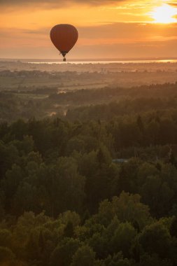 Parlak gün batımı nın arka planında ormanın üzerinde uçan turuncu bir hava balonu