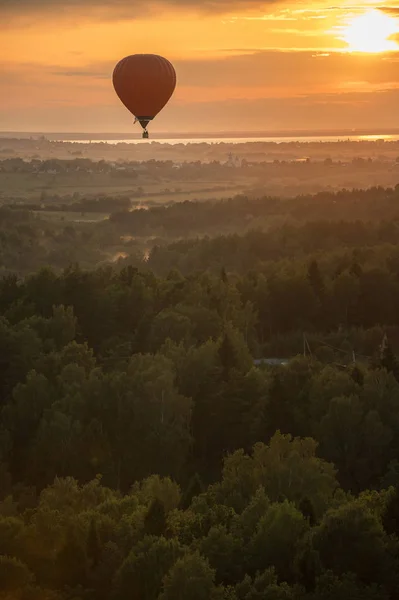 An orange air balloon flying over the forest on a background of bright sunset — Stock Photo, Image