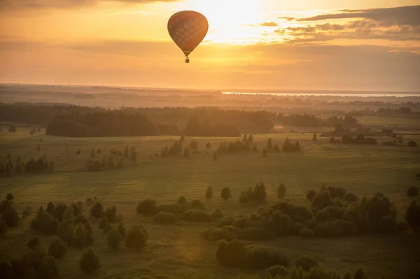 A colorful air balloon flying over the field - bright yellow sunset — Stock Photo, Image
