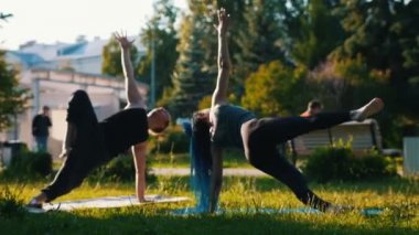 Parkta bir adam ile yoga egzersizleri yapıyor iki genç çekici kadın bir groop - Bir kadın uzun mavi dreadlocks var