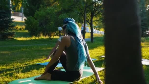 Dos mujeres jóvenes haciendo diferentes ejercicios de yoga con entrenador en el parque - Una mujer tiene rastas azules largas — Vídeo de stock