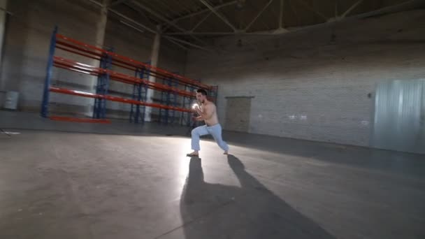 Un homme faisant des éléments de capoeira dans la pièce avec sol en béton et murs de briques — Video