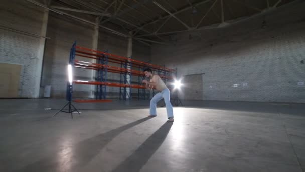 Egy ember csinál különböző capoeira elemeket a szobában betonozott padló, tégla falak és erős fény — Stock videók
