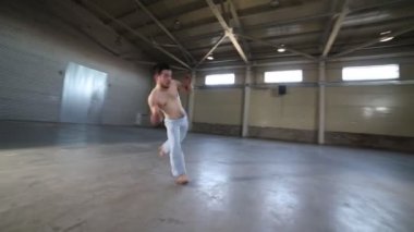 Beton zemin, tuğla duvarlar ve parlak ışık ile odada capoeira elemanları yapan bir adam