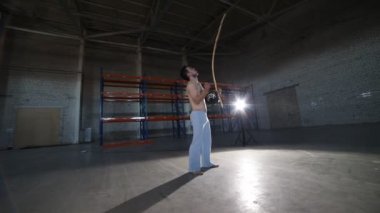 Beton zemin ve tuğla duvarlar ile odada capoeira elemanları yaptıktan sonra ulusal Brezilyalı enstrüman berimbau oynayan genç atletik adam