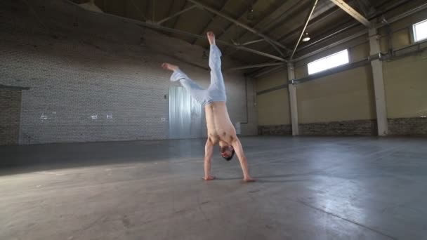 Mann springt auf seine Hände und hebt die Füße hoch und bleibt auf ihnen - zeigt Capoeira-Elemente — Stockvideo