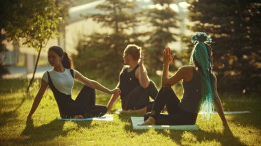 İki kadın - biri mavi saçlı - Ve parkta yoga egzersizleri yapan bir adam parlak yeşil ağaçlarla çevrili