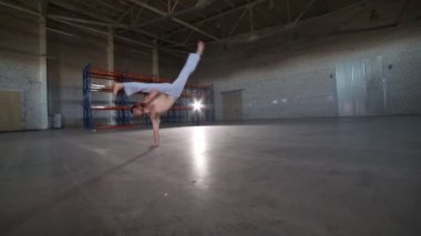 Bir adam farklı capoeira elemanları yapıyor - elinde kalan ve bir cartwheel yapıyor - beton zemin, tuğla duvarlar ve parlak ışık ile odada