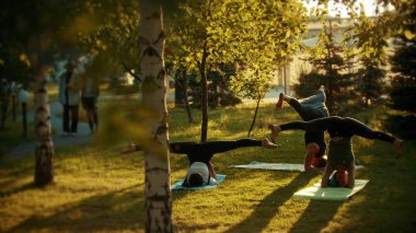 İki genç uygun kadın ve parlak yeşil ağaçlar ve geçit yakınındaki parkta yoga yapan bir adam - headstands doing