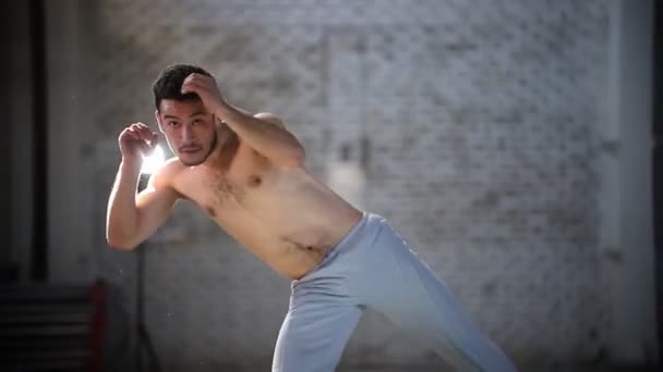 Homem atlético fazendo exercícios de capoeira - girando e levantando a perna em uma sala com paredes de tijolo — Vídeo de Stock