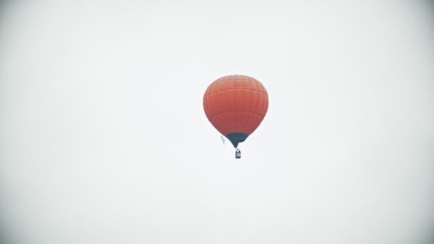 An orange air balloon flying on a background of white overcast sky — Stock Video