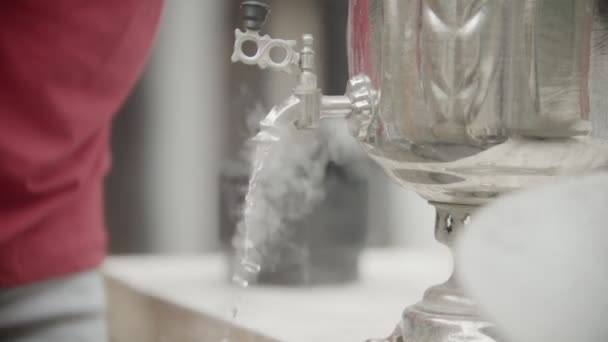 Кипляча вода, що спускається з великого металевого самовара з чоловічим силуетом на задньому плані — стокове відео