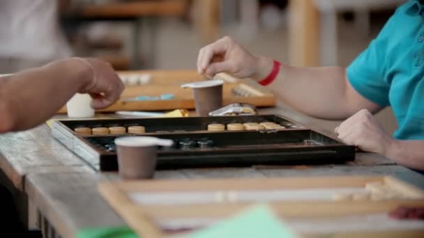 Twee mannen spelen backgammon aan de tafel buitenshuis-een man gooit een dobbelsteen-twee kopjes zijn naast hen — Stockvideo