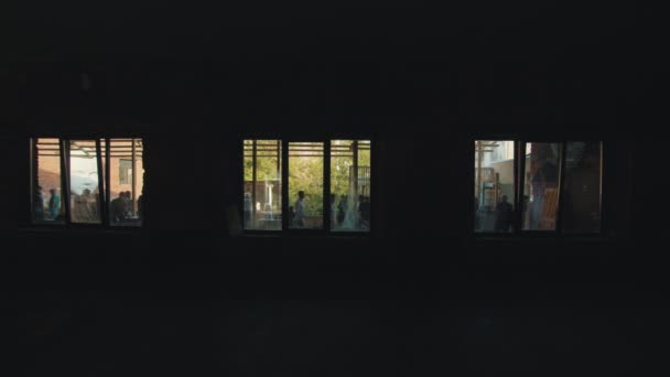 A dark room with three windows looking outside - people have a meeting outside — Stock Video