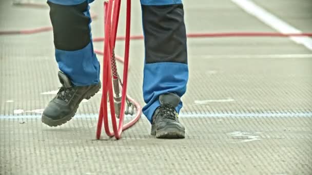 Un hombre que lleva una manguera con botas y pantalones grandes — Vídeo de stock