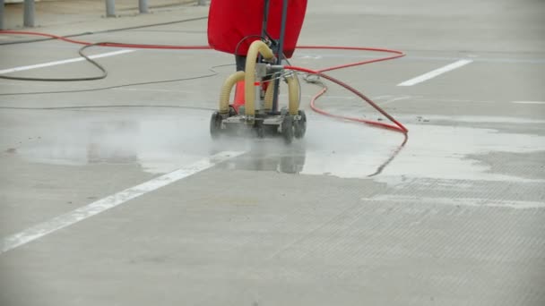 Een oude vrouw werknemer reiniging van het asfalt met behulp van water-luchthaven veld — Stockvideo
