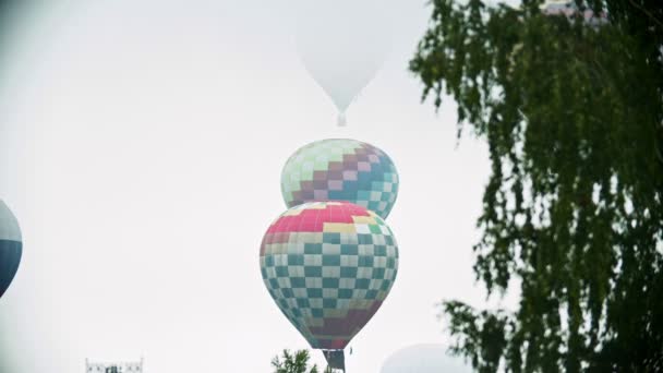 Διάφορα πολύχρωμα μπαλόνια αέρα απογειώμαστε πάνω από το χωράφι σε ένα φόντο του λευκού ουρανού — Αρχείο Βίντεο