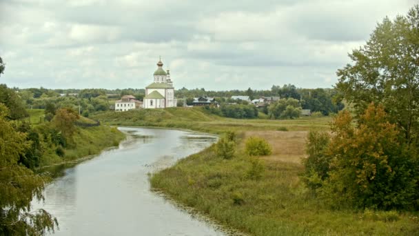 Fehér keresztény templom a településen-vízpatak az előtérben-Suzdal, Oroszország — Stock videók