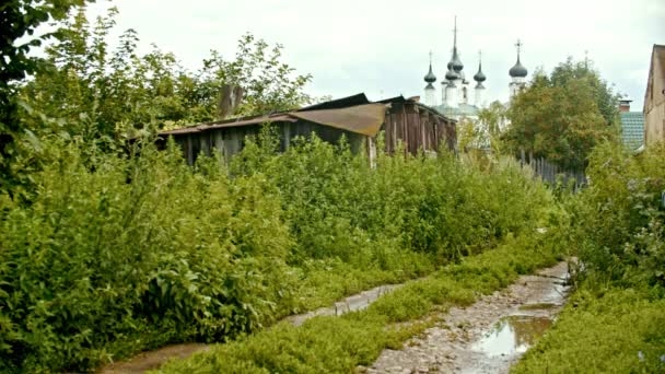 Вид на маленькую деревню - старый дом и мокрую тропу на переднем плане - большая церковь на заднем плане - Суздаль, Россия — стоковое видео