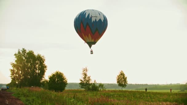 Un globo grande y colorido volando sobre el prado usando tecnología de calor - puesta de sol — Vídeos de Stock