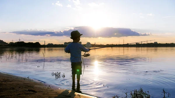 Ein kleiner Junge beim Angeln am Ufer des Flusses bei Sonnenuntergang — Stockfoto