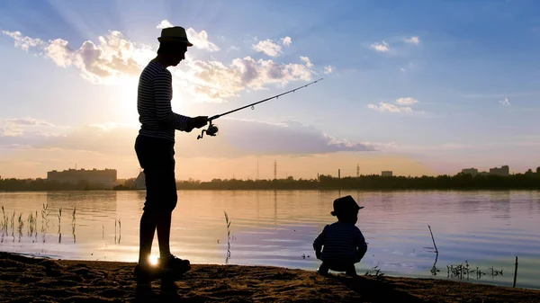 父亲和儿子在夕阳的光线下在河岸上钓鱼 — 图库照片