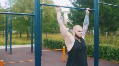 Bir spor katında barda asılı dövmeler ile güçlü sakallı adam