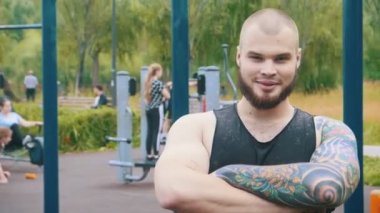 Güçlü bir sakallı gülümseyen adam dövme ayakta spor zemin açık havada-silah ile kamera görünümlü geçti