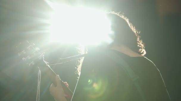 Een jonge man met lange haren spelen een lied op zijn prestaties-Bright Ray van licht — Stockvideo