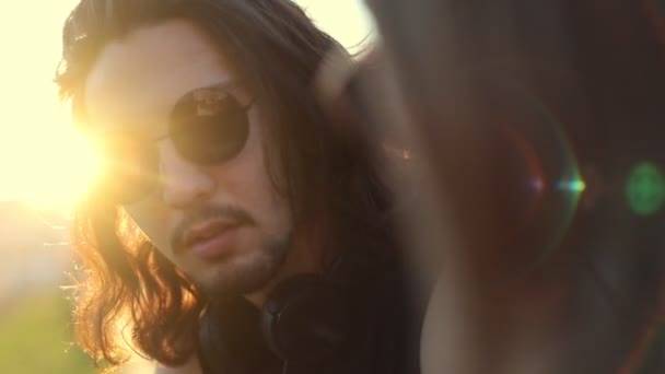 Un homme aux longs cheveux ondulés dans des lunettes - un jeune couple qui se parle à l'extérieur — Video