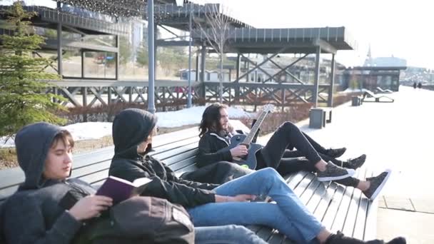 Jonge vrienden koelen op een bench-het lezen van een boek en het afstemmen van de gitaar — Stockvideo