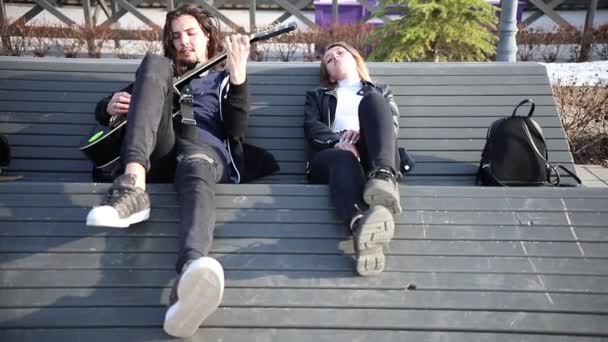 Mladý pár ležící na lavičce-muž hrající na kytaru — Stock video