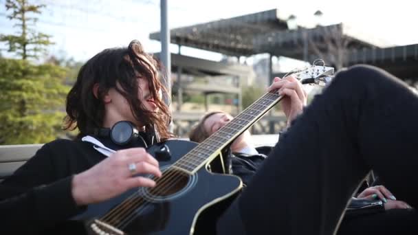 Ungt par sitter på bänken-en man som spelar gitarr och sjunger — Stockvideo