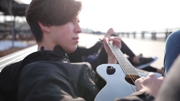 Un jeune homme allongé sur un banc et jouant de la guitare à l'extérieur — Video