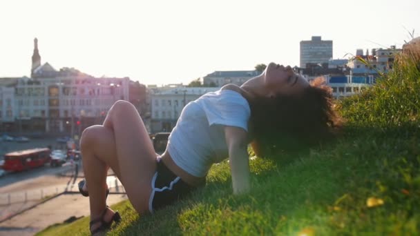 Atractiva mulata flaca tumbada en la hierba y realizando elementos de baile de striptease - flexiona su espalda y sintiéndose — Vídeos de Stock