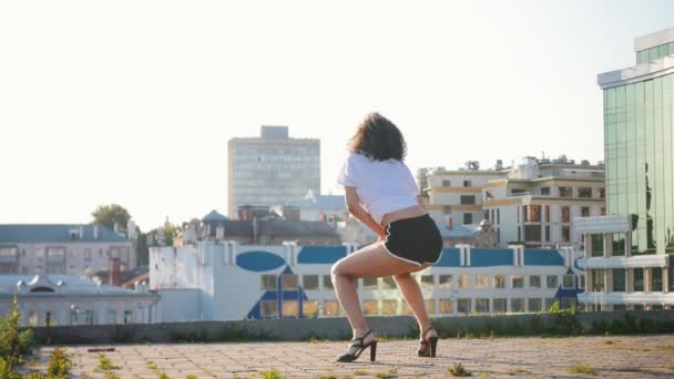 Atractiva mulata joven sexy bailando en tacones altos en el techo twerking y tumbado en el suelo — Vídeo de stock