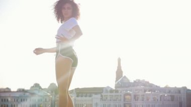 Modern binaların bir arka planda kıvırcık saç dans ile çekici melez genç kadın-parlak güneş ışığı