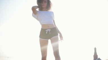 Modern binaların bir arka planda kıvırcık saç dans ile çekici melez genç kadın-squat üzerine düşen