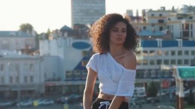 Kıvırcık saçlı dans ve modern binaların bir arka planda bir izleyici ile flört ile çekici melez genç kadın