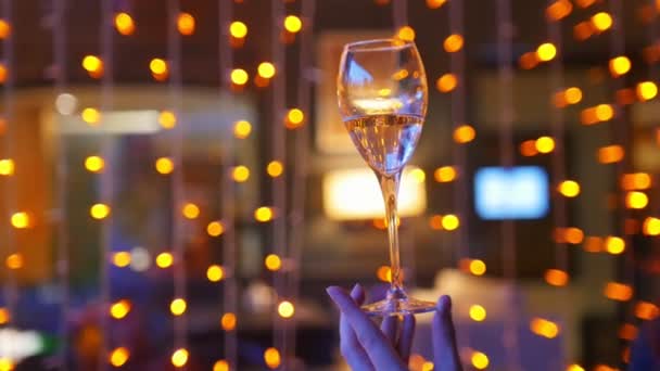 A woman hand holding a glass of champagne on a background of orange lights — Stock Video