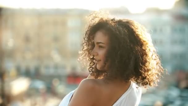 Молодая привлекательная женщина с вьющимися волосами флиртует с кем-то на городском фоне — стоковое видео